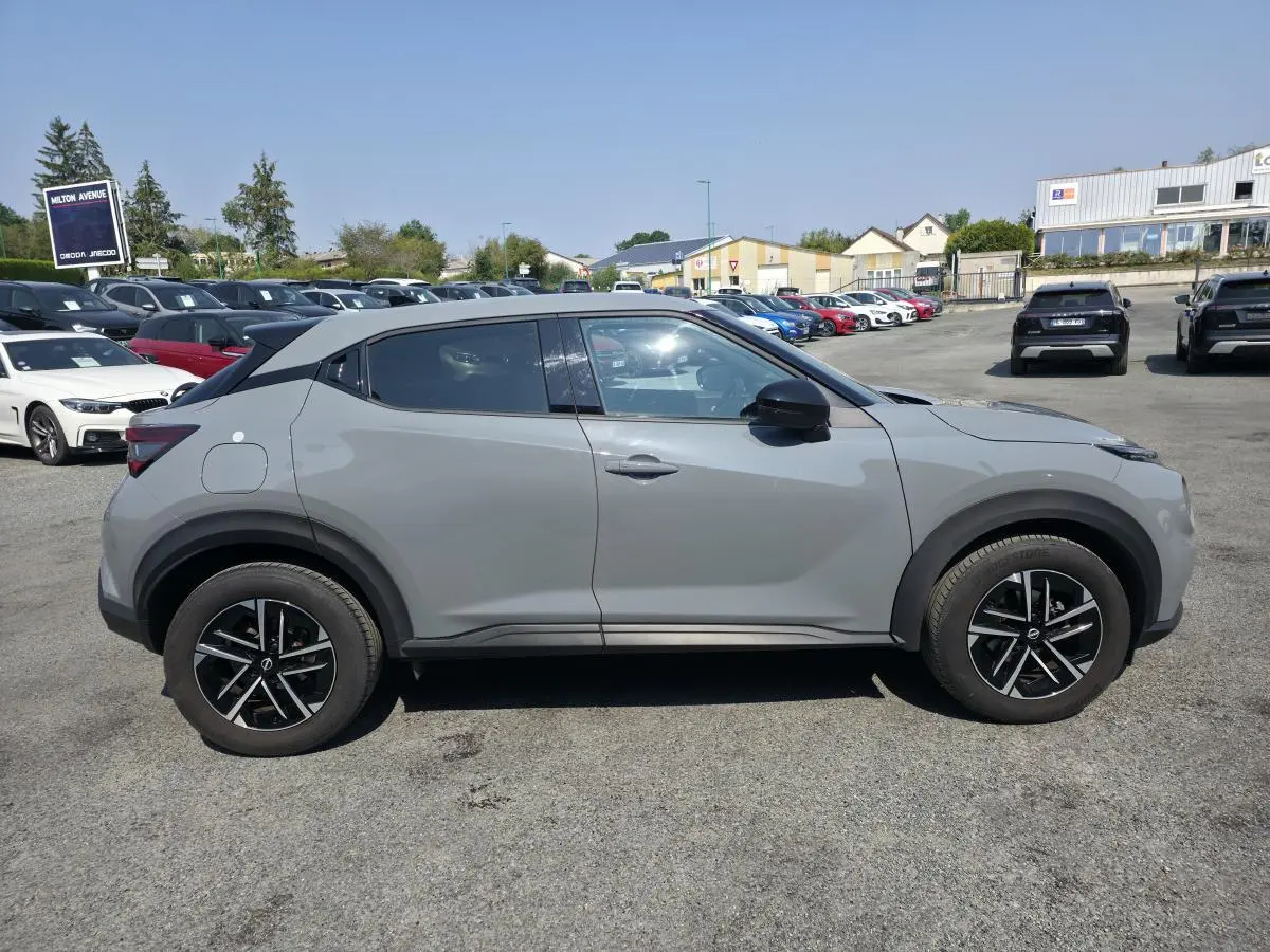 Vue de profil côté gauche d'un Nissan Juke gris métallisé 2025 avec jantes alliage noires et toit noir.