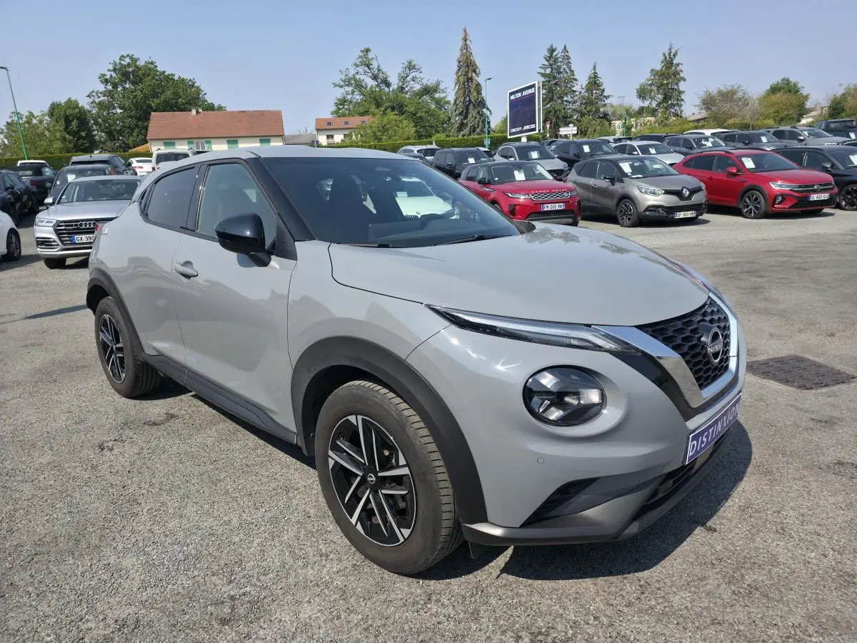 Nissan Juke gris métallisé vue 3/4 avant droit avec jantes alliage noires et coques de rétroviseurs noires.