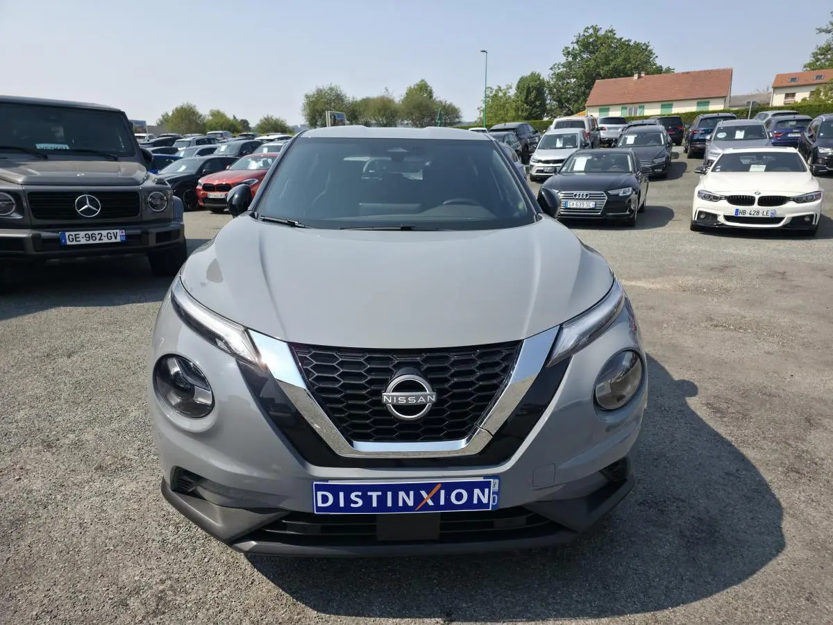 Vue avant d'un Nissan Juke gris métallisé 2025 avec calandre en V chromée et logo Nissan visible.