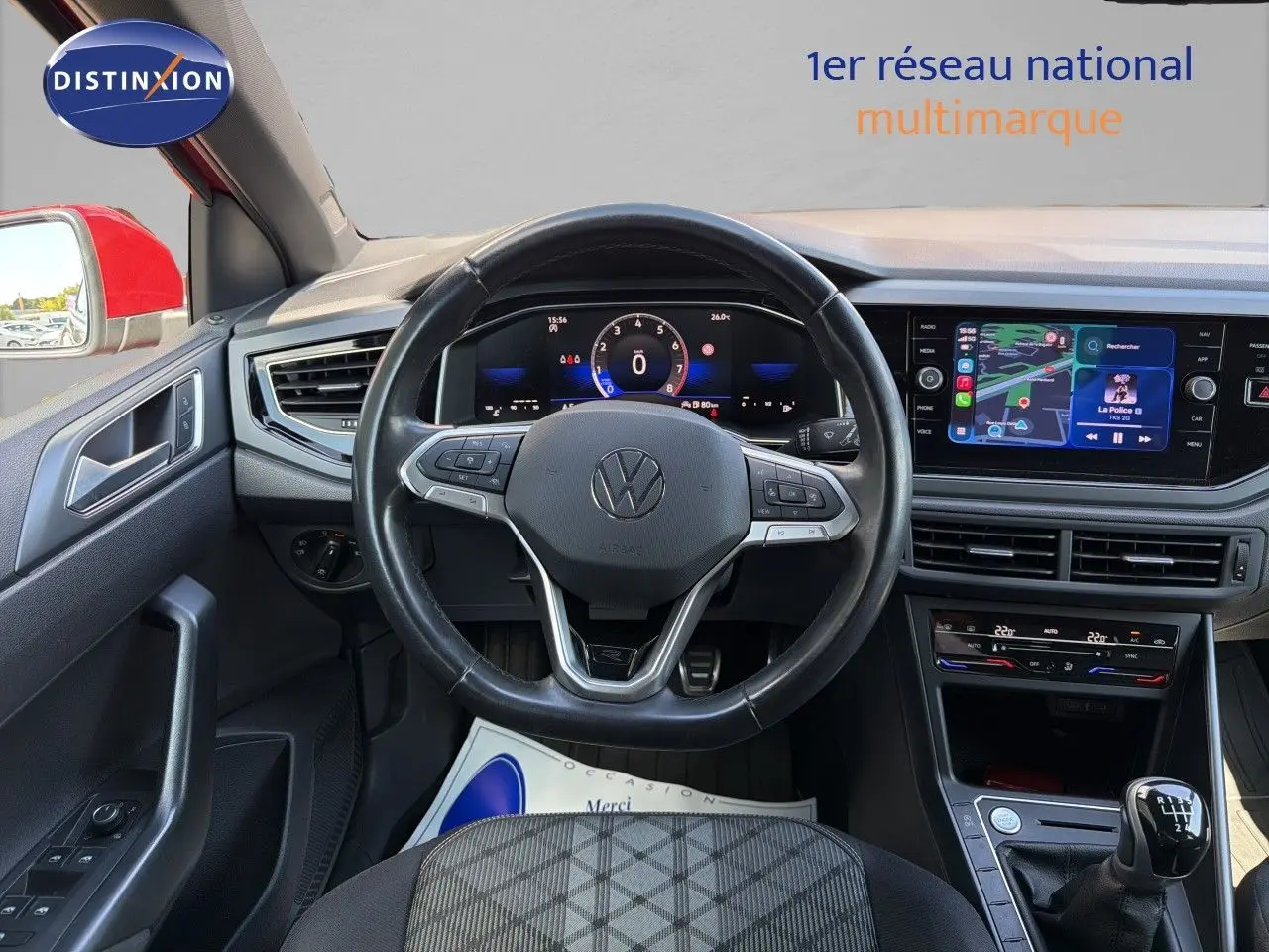 Vue intérieure centrée sur le volant et tableau de bord d'une Volkswagen Polo rouge Roi avec boîte manuelle, écran tactile et climatisation.