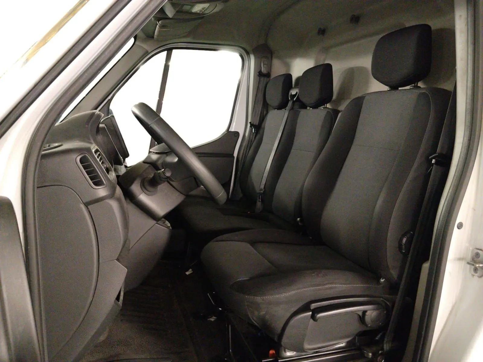 Vue intérieure côté conducteur du Renault Master blanc 2023, montrant les trois sièges noirs et le tableau de bord.