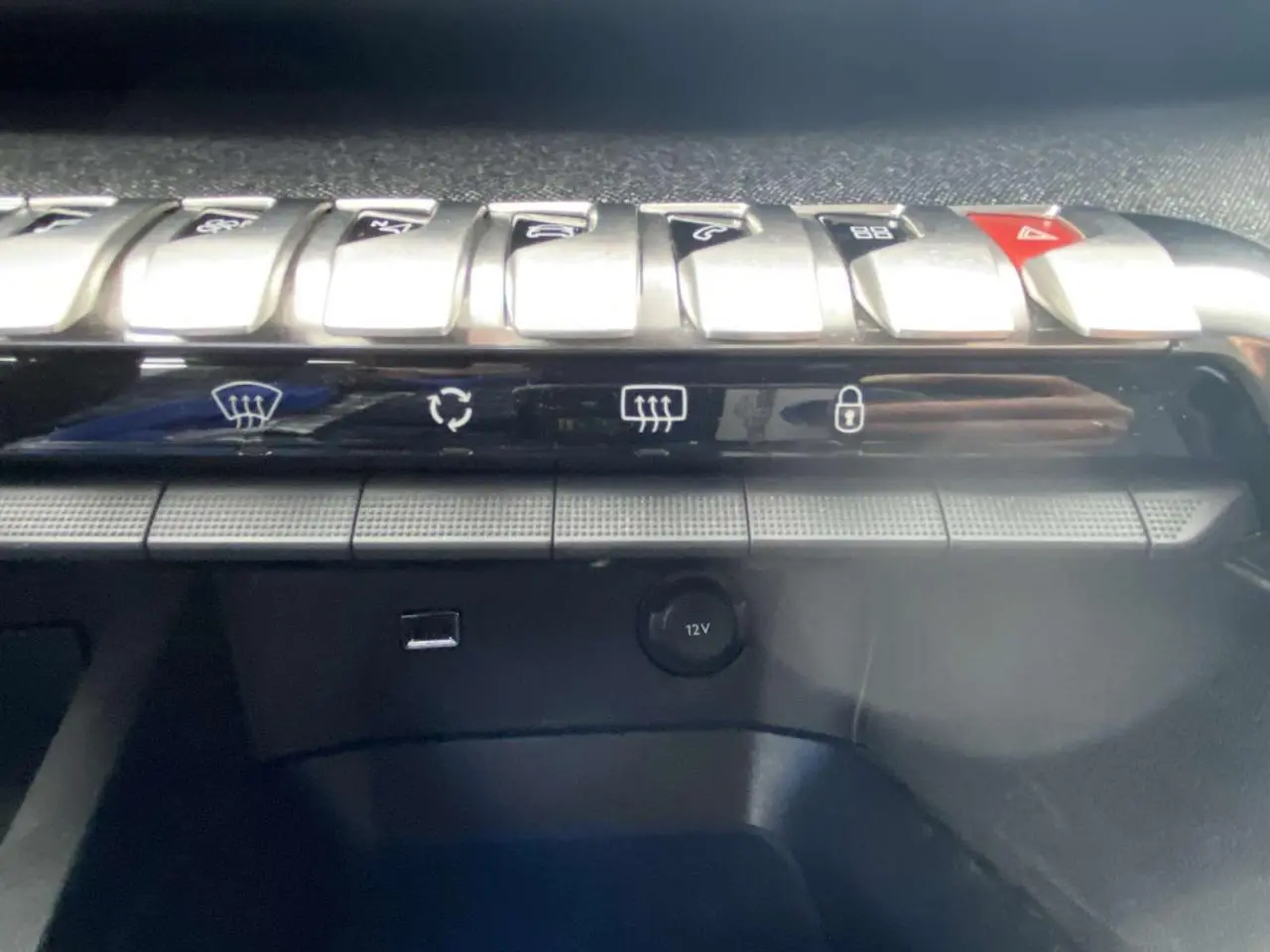 Gros plan sur la rangée de commandes chromées et la prise 12V du tableau de bord du Peugeot 3008 Allure blanc nacré 2017.