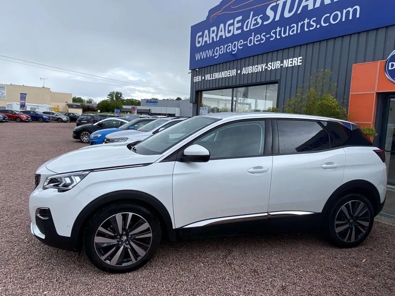 Profil droit du Peugeot 3008 blanc nacré 2017 avec jantes alliage 19 pouces et vitres surteintées, stationné devant un garage.