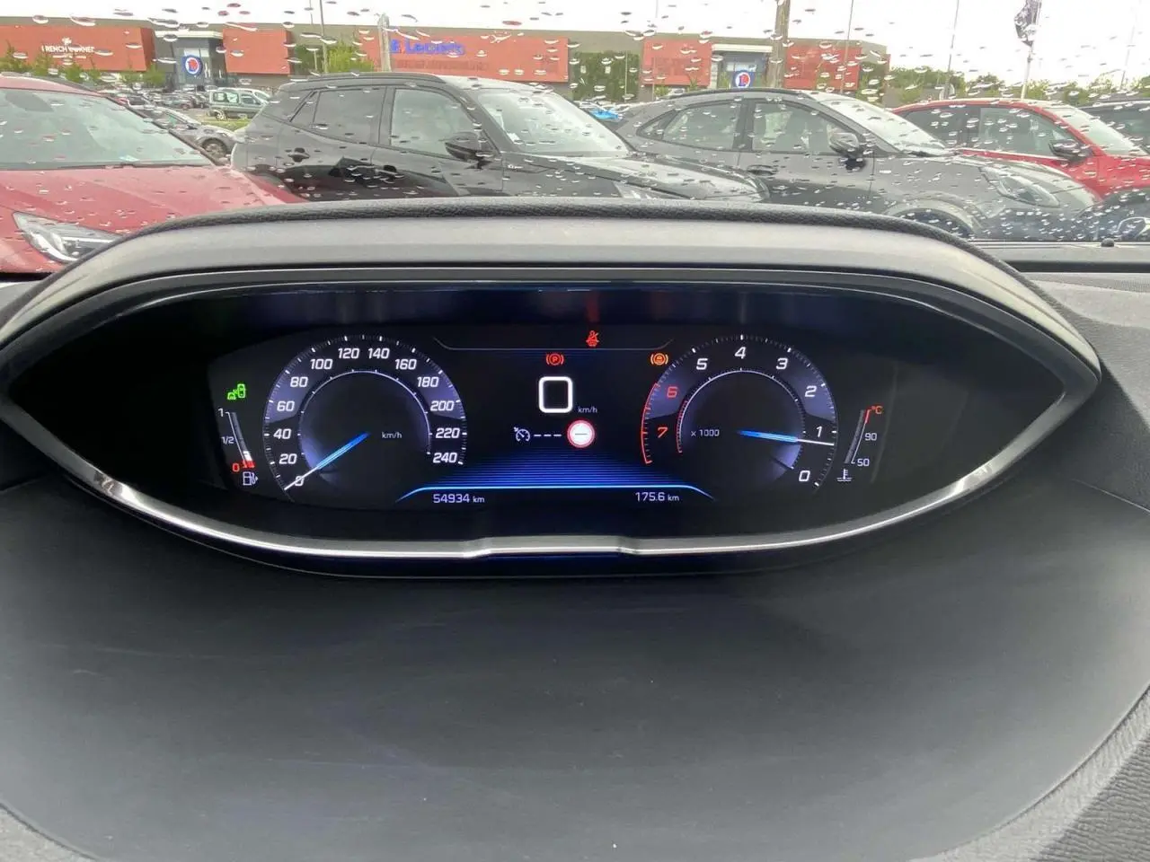 Tableau de bord numérique du Peugeot 3008 blanc 2017, affichant vitesse et compte-tours, avec pluie en arrière-plan.