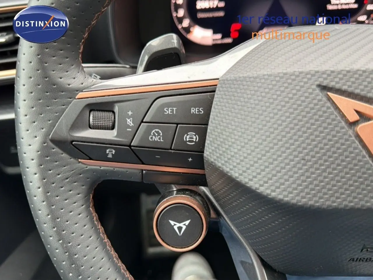 Gros plan sur le volant en cuir perforé noir du CUPRA Formentor blanc neige métal, avec commandes intégrées et logo distinctif.