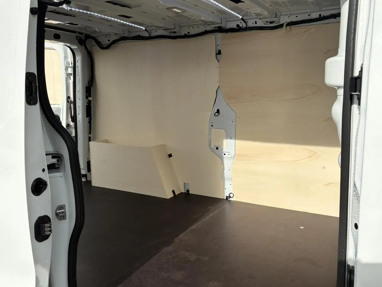 Vue intérieure côté droit du fourgon Renault Trafic blanc glacier avec habillage bois complet et plancher noir.