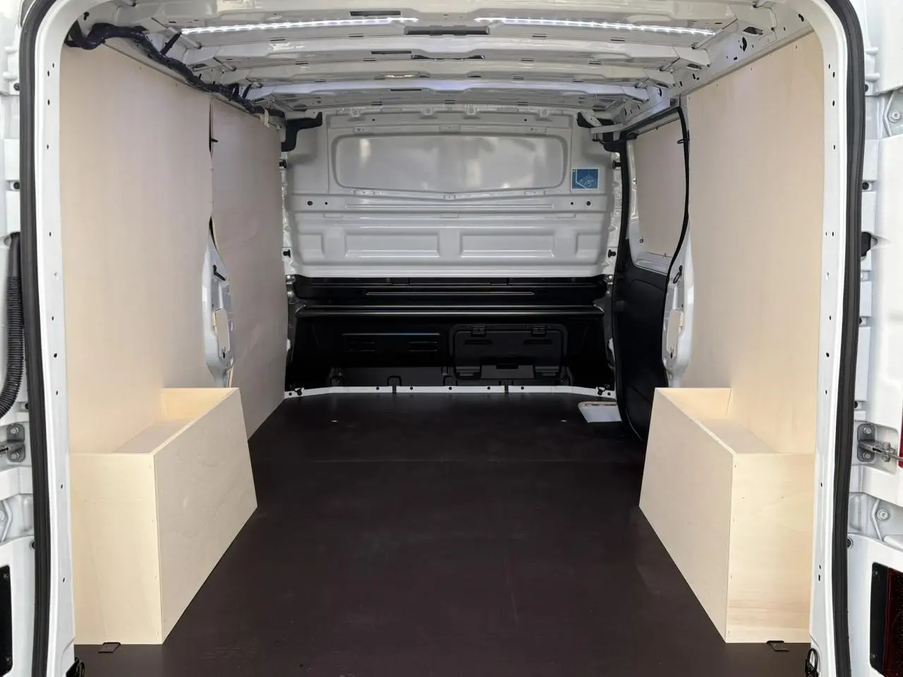 Intérieur arrière du Renault Trafic Fourgon blanc glacier, vue de la zone de chargement avec habillage bois complet.