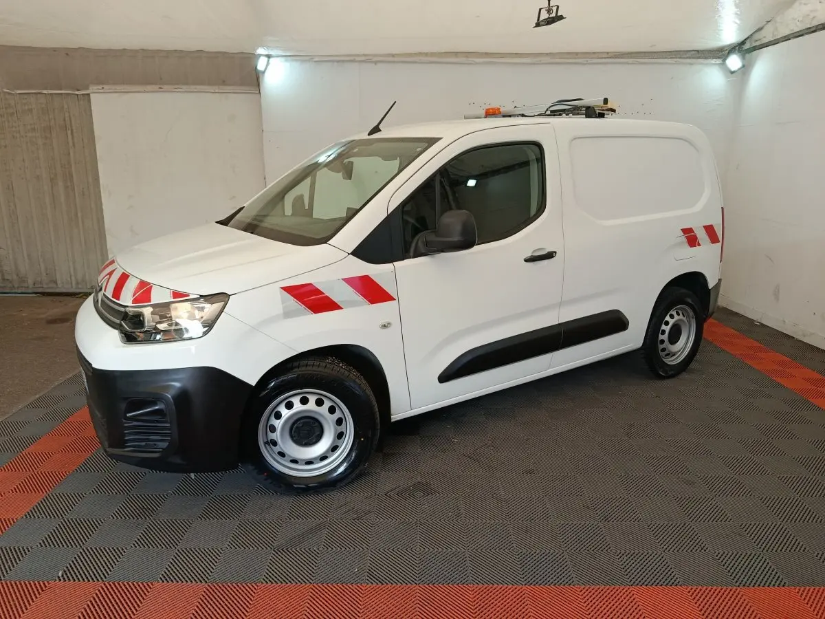 Vue 3/4 avant droite d'un Citroën Berlingo blanc 2021 avec bandes rouges réfléchissantes et toit équipé d'une rampe lumineuse.