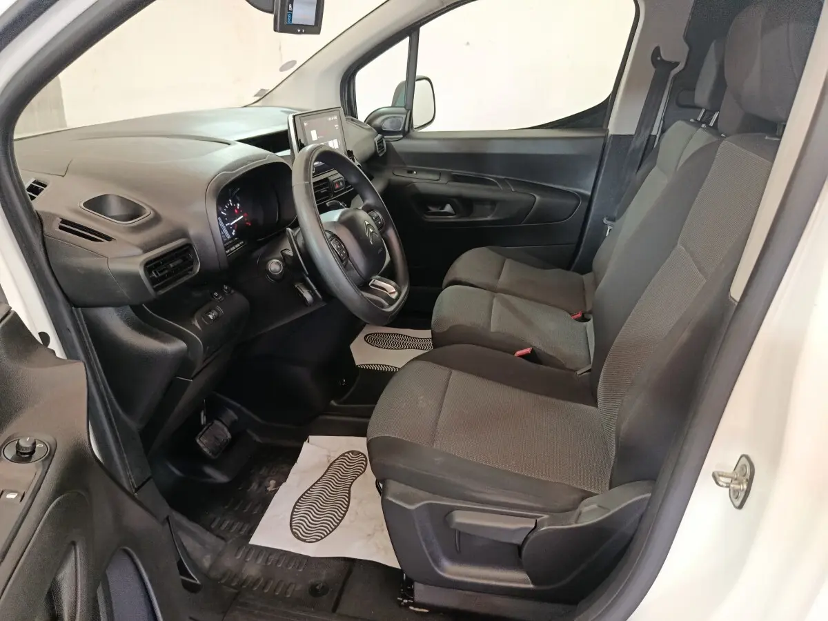 Vue intérieure côté conducteur du Citroën Berlingo blanc 2021, montrant le tableau de bord et les sièges avant gris foncé.