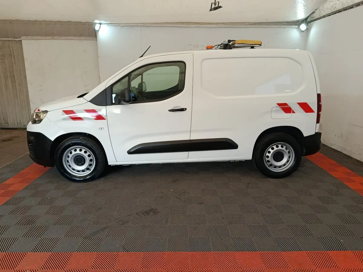 Vue de profil côté gauche d’un utilitaire Citroën Berlingo blanc 2021 avec bandes réfléchissantes rouges et gyrophare sur le toit.