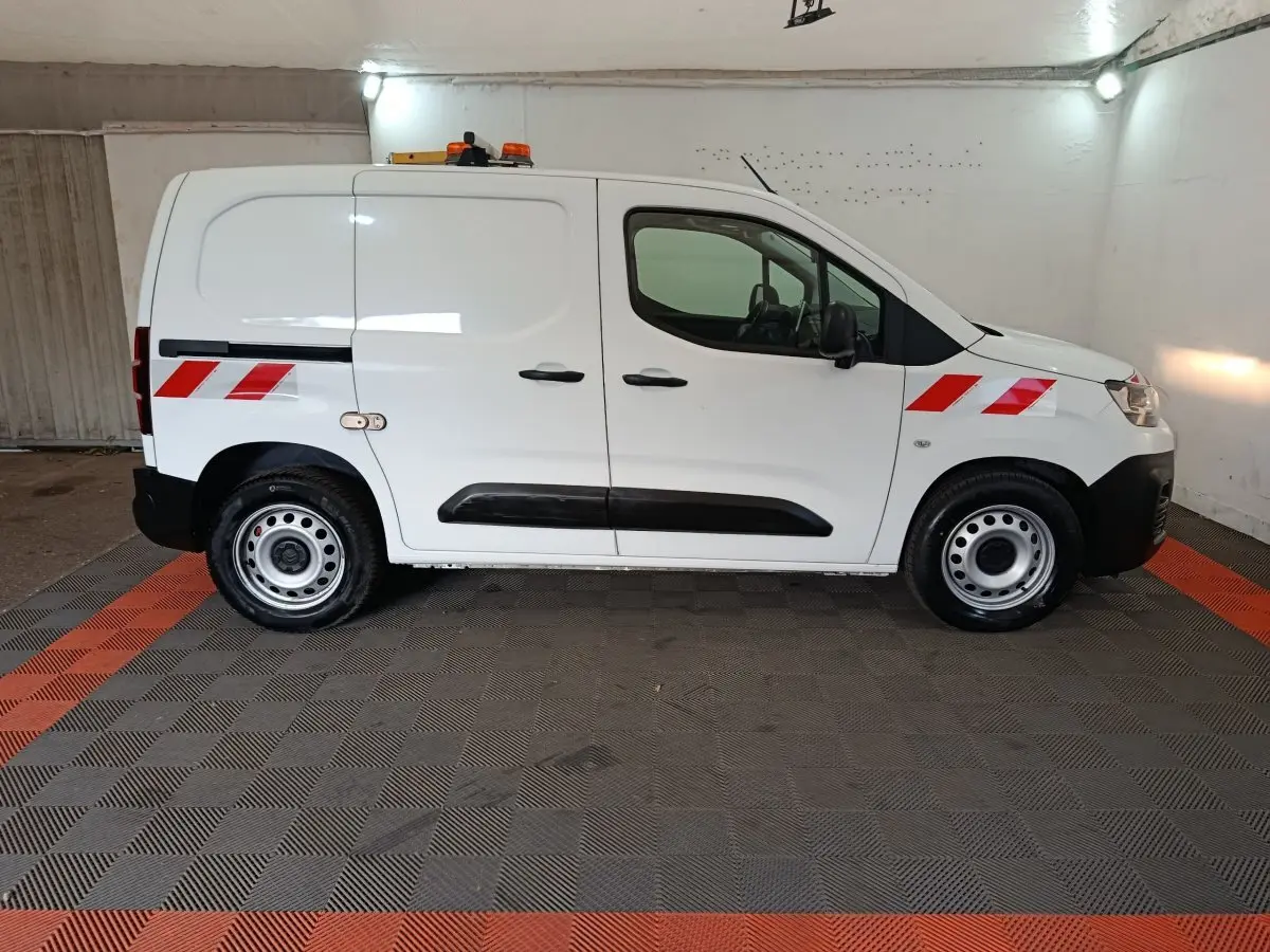 Vue de profil côté droit d'un Citroën Berlingo blanc 2021 avec bandes réfléchissantes rouges et gyrophare orange sur le toit.