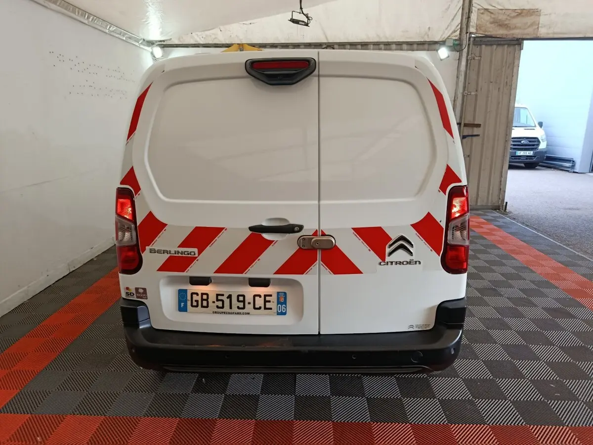 Vue arrière d’un Citroën Berlingo blanc 2021 avec bandes rouges diagonales de sécurité et plaque d’immatriculation française.