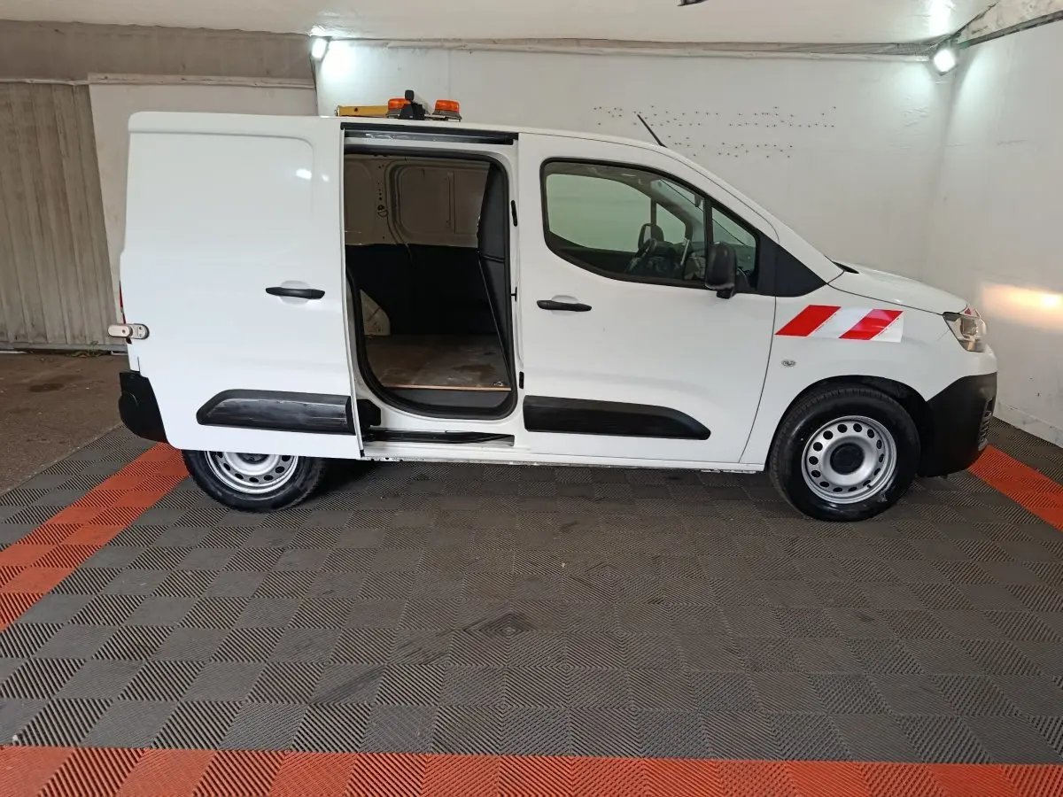 Vue de profil côté droit d’un Citroën Berlingo blanc 2021 avec porte latérale coulissante ouverte et bandes rouges réfléchissantes sur l’aile avant.