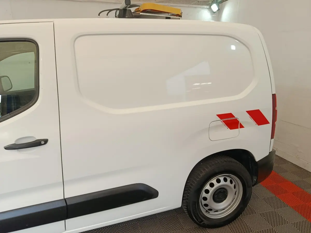 Vue latérale droite d’un Citroën Berlingo blanc 2021 avec bandes rouges réfléchissantes sur l’aile arrière.