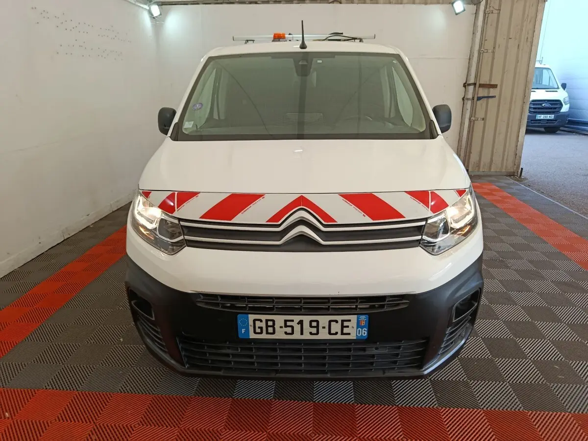 Vue avant d'un Citroën Berlingo blanc 2021 avec bande rouge et blanche réfléchissante sur le capot, en intérieur.