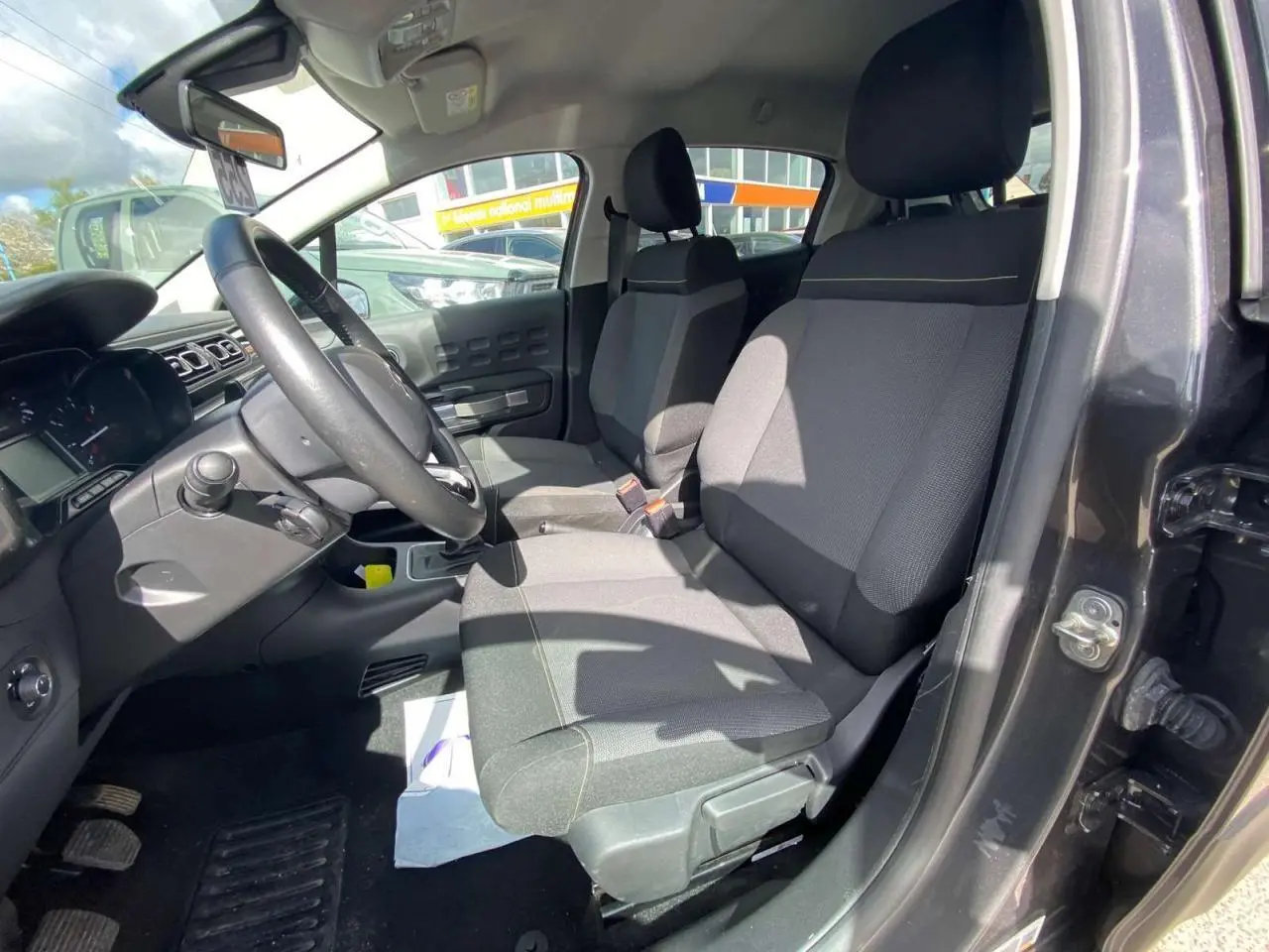 Vue intérieure côté conducteur de la Citroën C3 gris platinium, montrant les sièges avant et le volant noir.