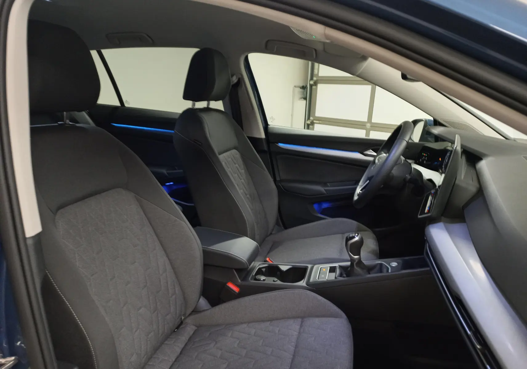 Vue intérieure côté conducteur de la Volkswagen Golf 1.5 TSI 116 BVM6 VW Edition avec sièges tissu gris et éclairage d'ambiance bleu