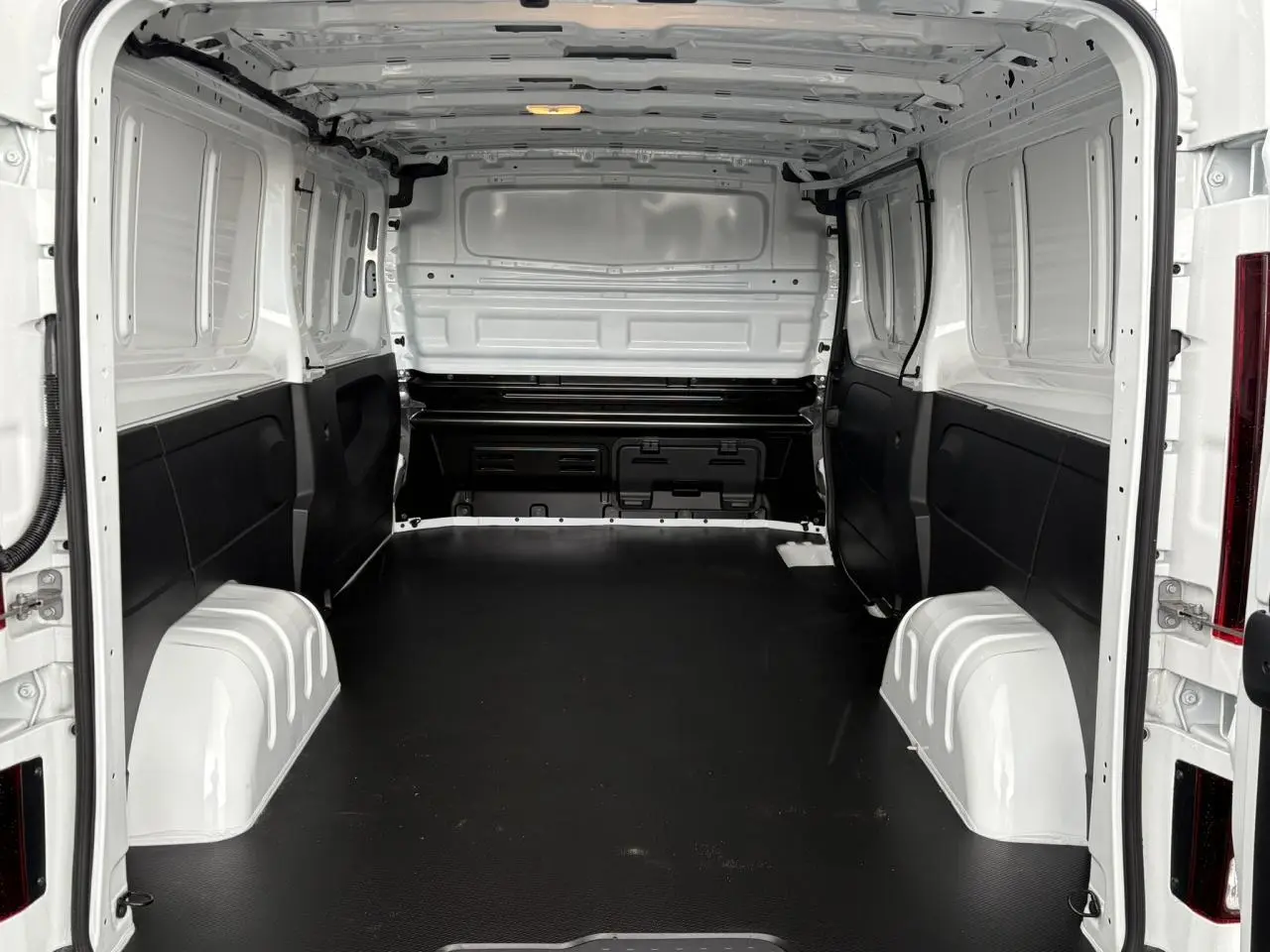 Vue intérieure arrière du Renault Trafic Fourgon blanc Glacier, montrant l'espace de chargement avec plancher bois noir.