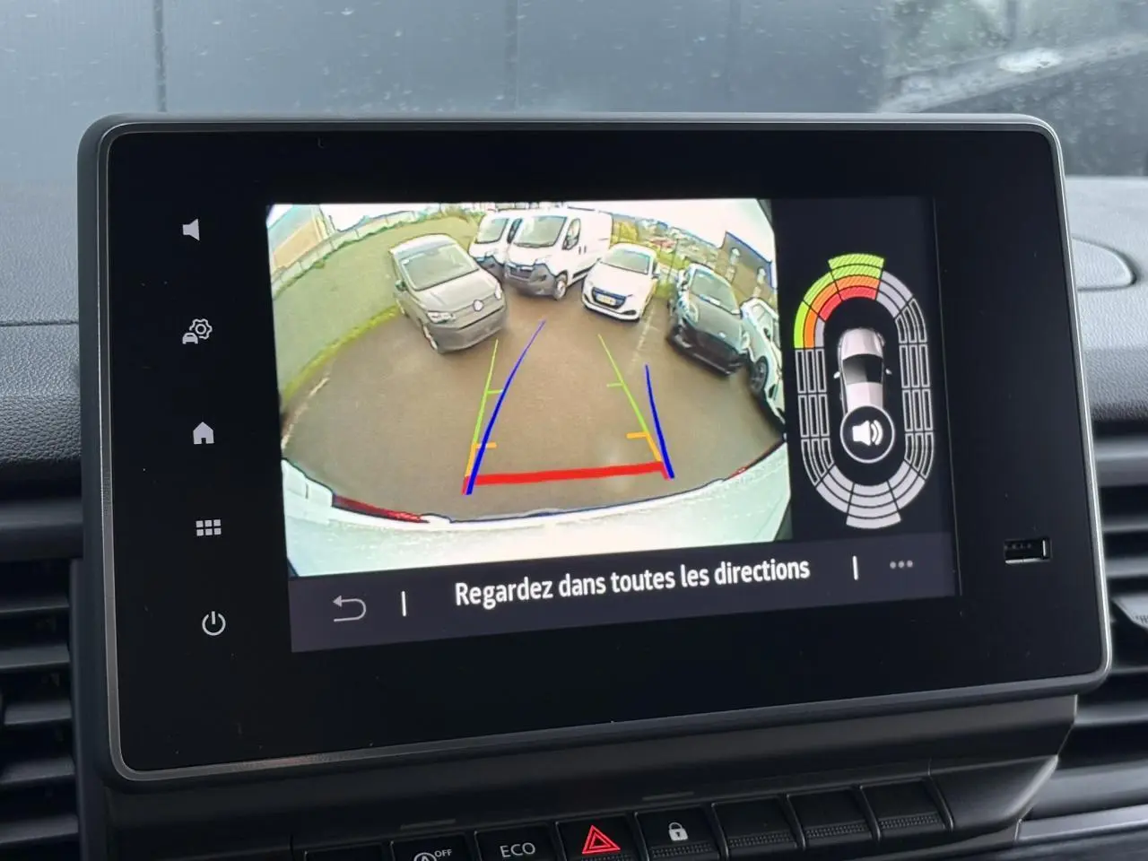 Vue de l'écran de la caméra de recul du Renault Trafic blanc, avec lignes de guidage colorées et véhicules en arrière-plan.