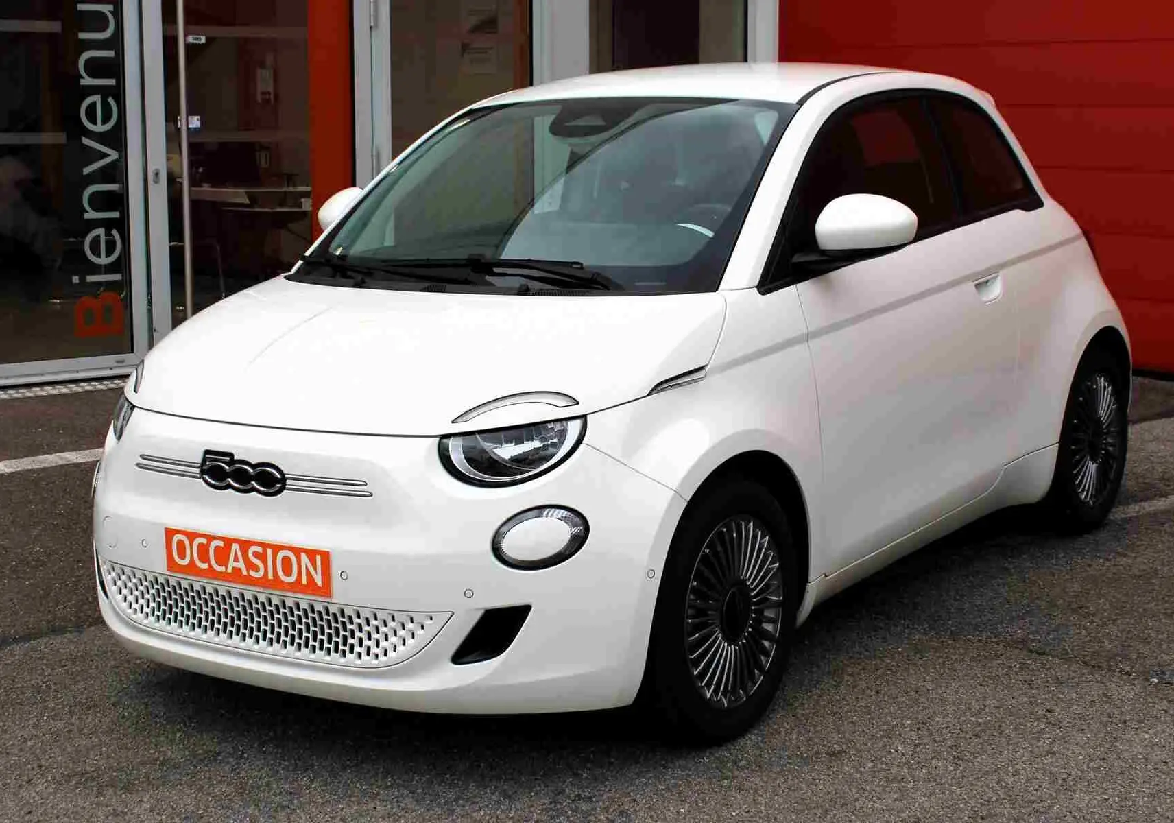 Fiat 500 électrique blanche vue 3/4 avant droit, avec jantes stylisées et plaque "OCCASION" orange visible.