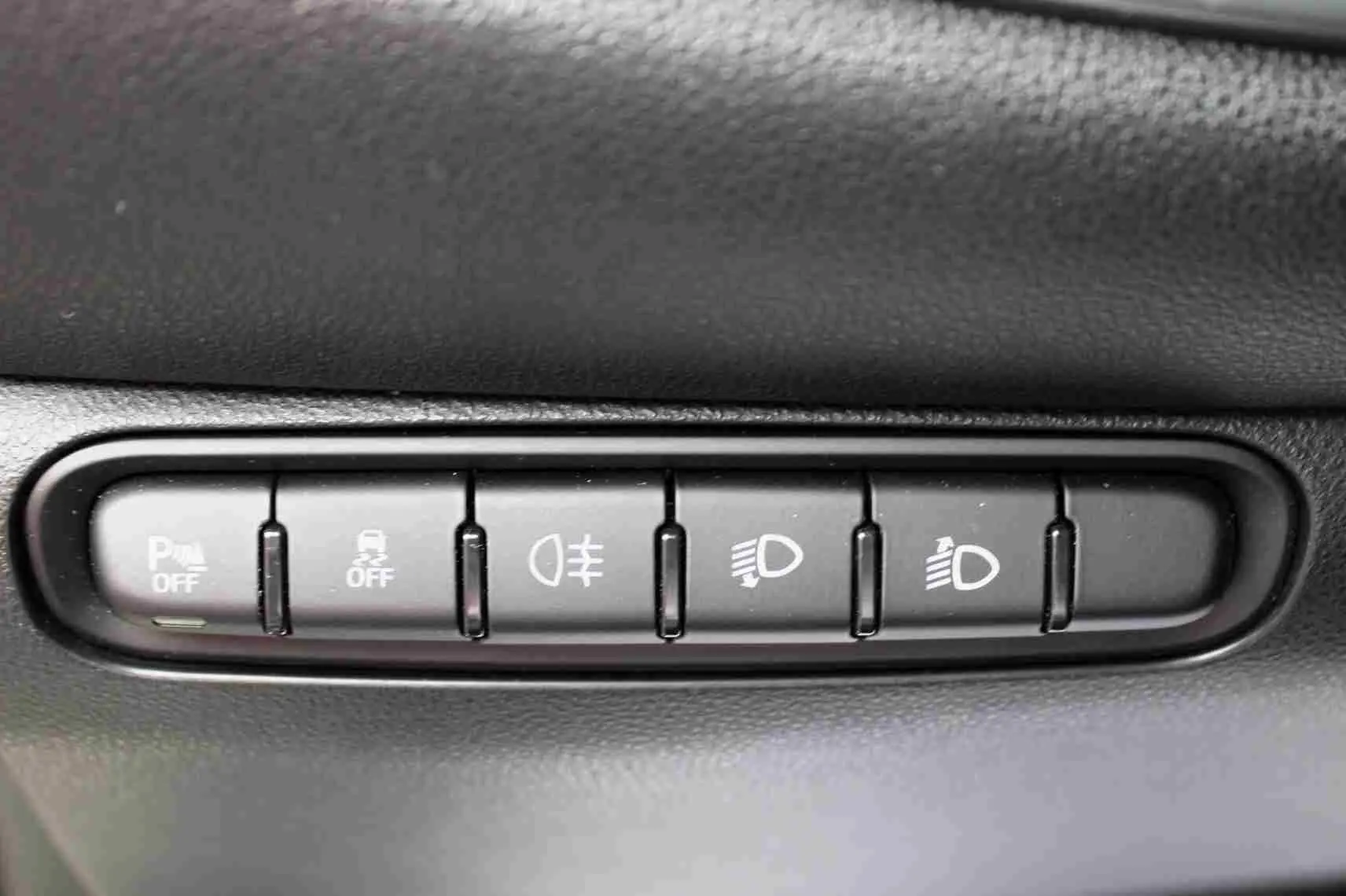 Gros plan sur les boutons de commande d’éclairage et d’aide à la conduite dans une Fiat 500 électrique blanche, intérieur noir.
