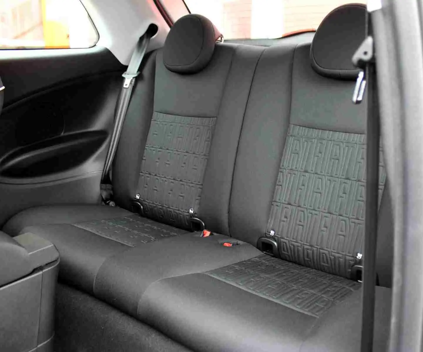 Vue intérieure de la banquette arrière noire de la Fiat 500 électrique 2023 avec motifs FIAT embossés sur les sièges.