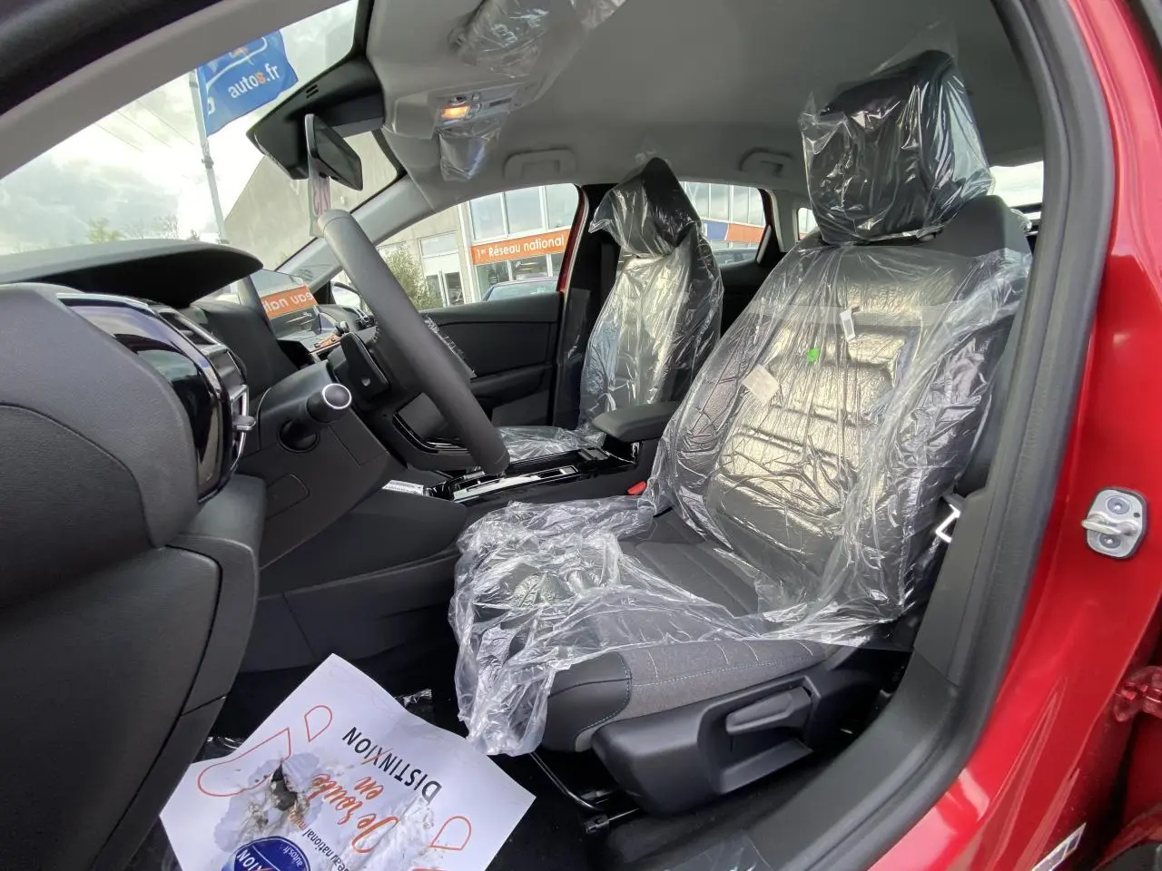 Vue intérieure côté conducteur de la Citroën C4 2023 rouge Elixir avec sièges protégés par film plastique.