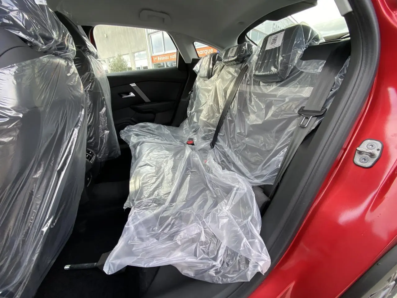Vue côté gauche arrière de l'intérieur d'une Citroën C4 rouge Elixir, sièges arrière protégés par housses plastiques.