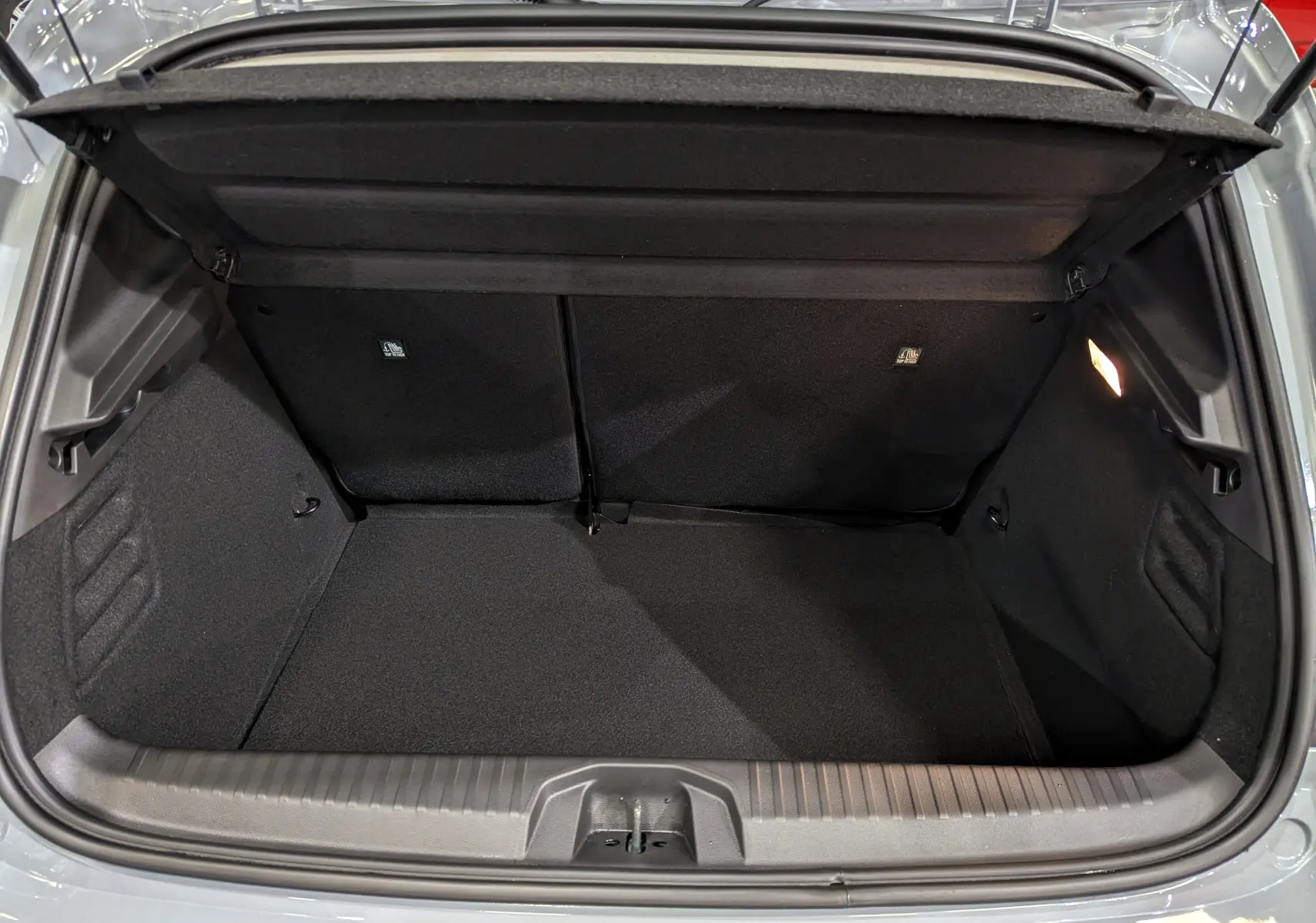 Coffre ouvert vu de dessus de la Renault Clio V Gris Rafale, montrant l’espace de rangement intérieur et l’éclairage à droite.