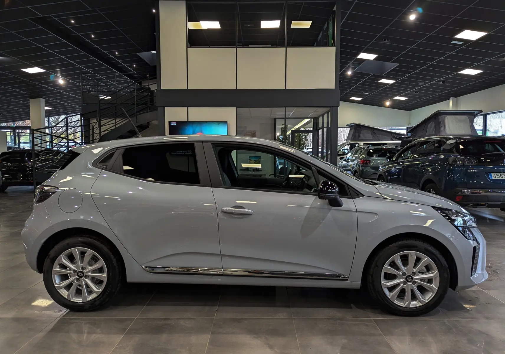 Profil côté gauche de la Renault Clio V gris Rafale 2025 en intérieur, avec jantes alliage et vitres teintées.