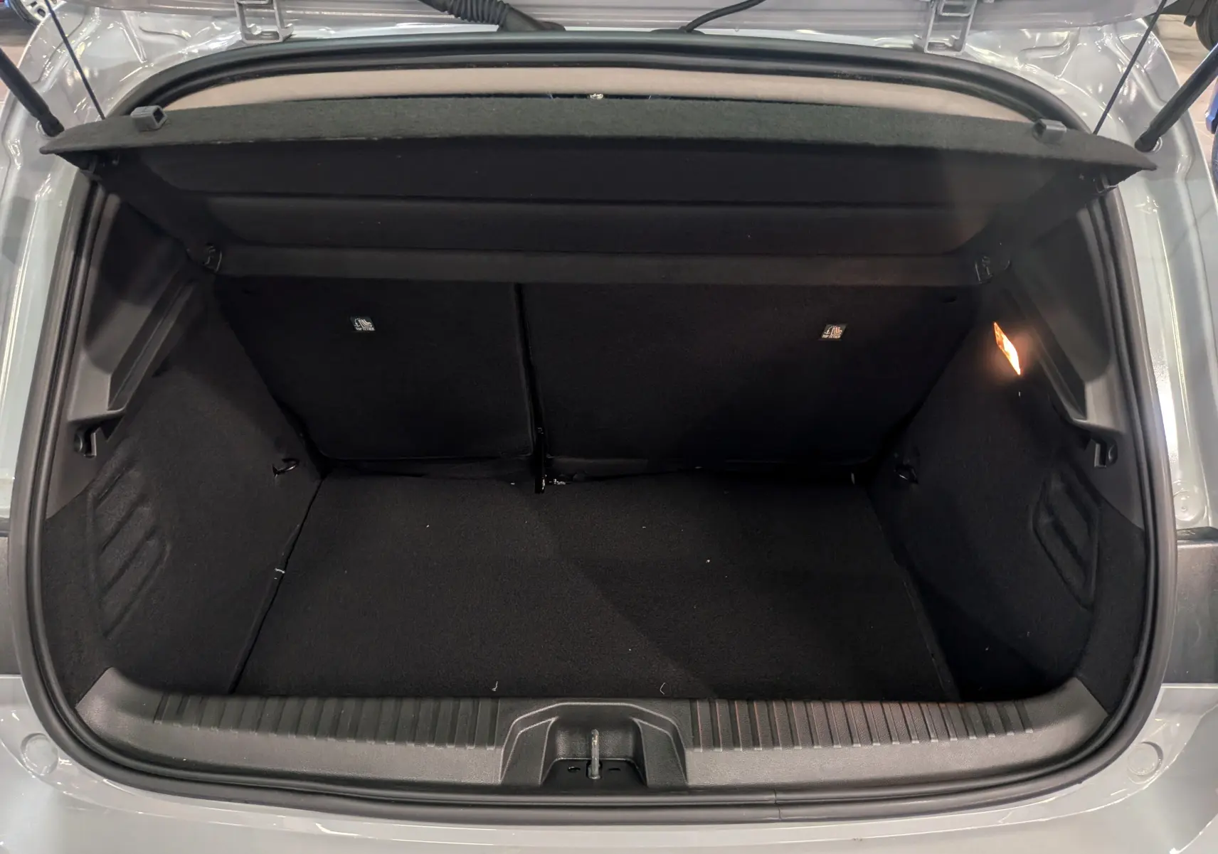 Coffre ouvert vu de l'arrière d'une Renault Clio V gris Rafale, montrant un espace de rangement propre et éclairé.