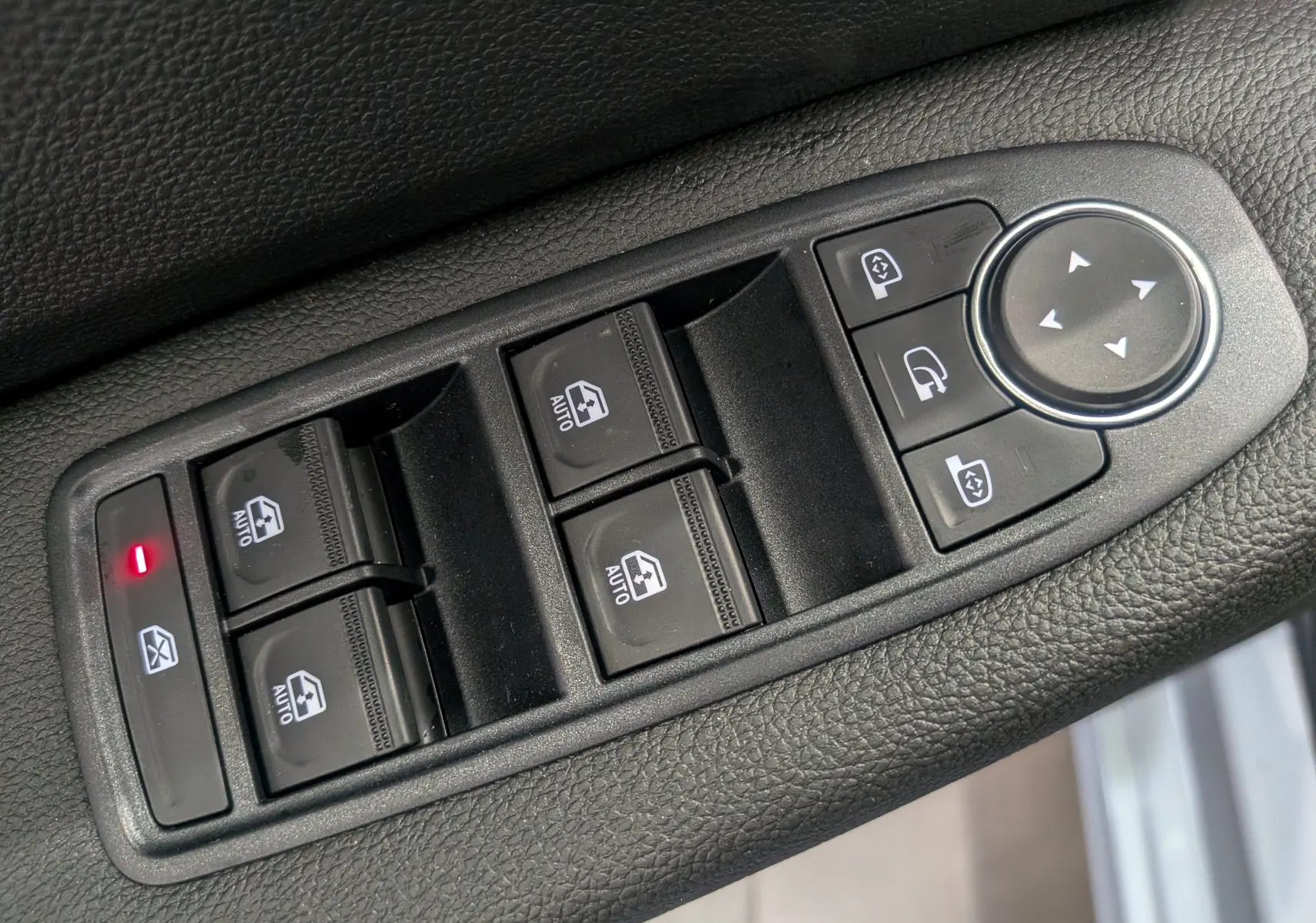 Gros plan sur les commandes de lève-vitres et rétroviseurs électriques sur la porte côté gauche d’une Renault Clio V gris Rafale.