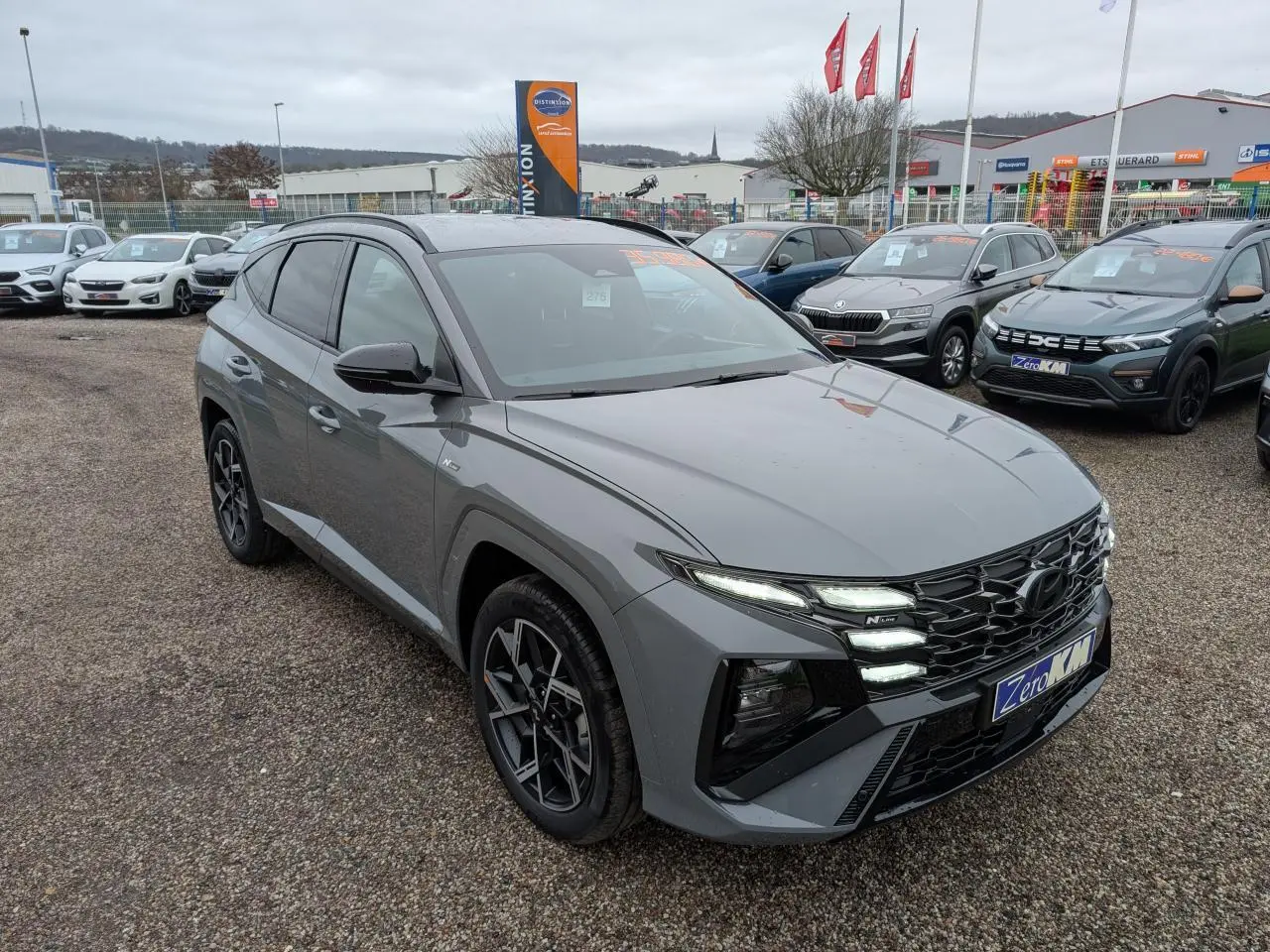 Vue 3/4 avant d'un Hyundai Tucson gris métallisé avec calandre noire N Line et jantes alliage 19 pouces sur parking.