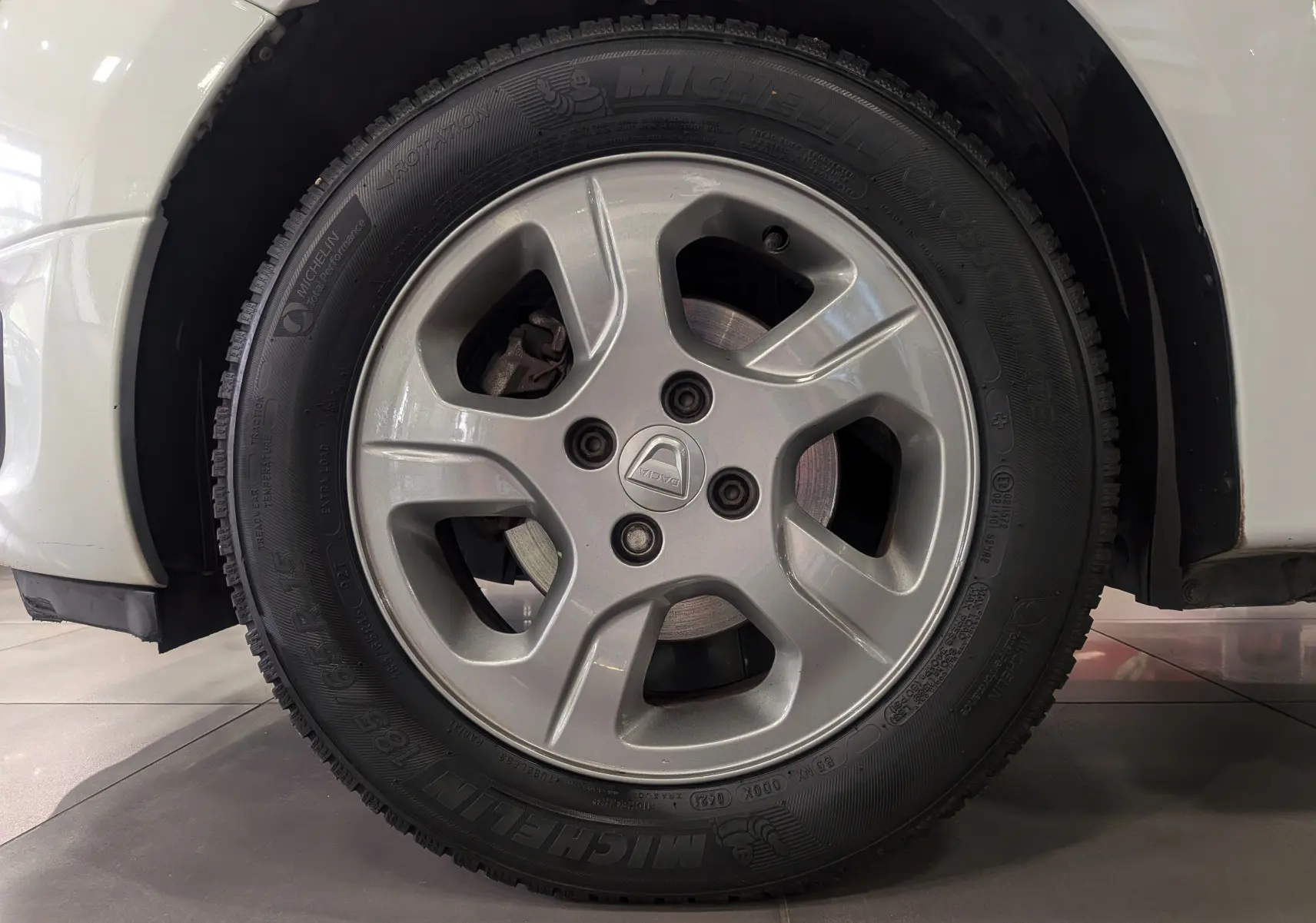 Gros plan sur la roue avant droite d'une Dacia Sandero blanc glacier, mettant en valeur le pneu et l'aile du véhicule.
