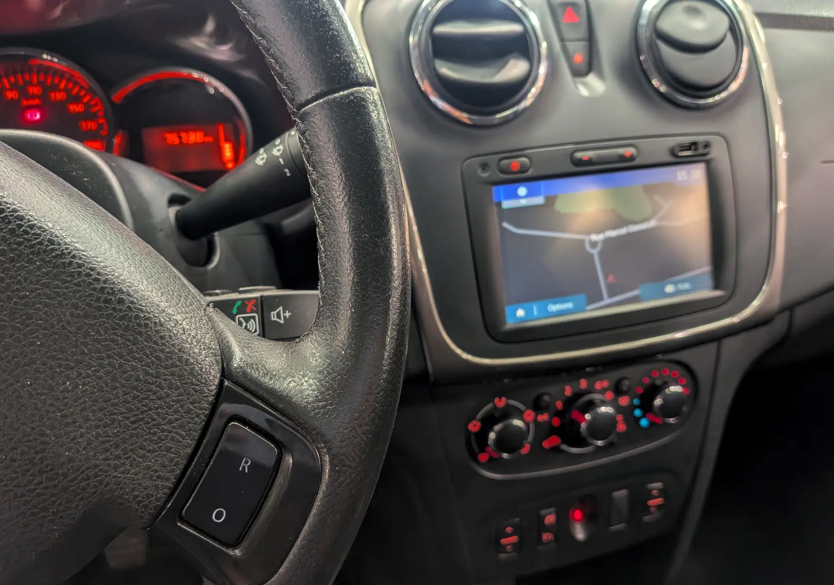 Intérieur de Dacia Sandero TCe 90 2015, vue sur le volant, tableau de bord et écran GPS tactile avec commandes climatiques.