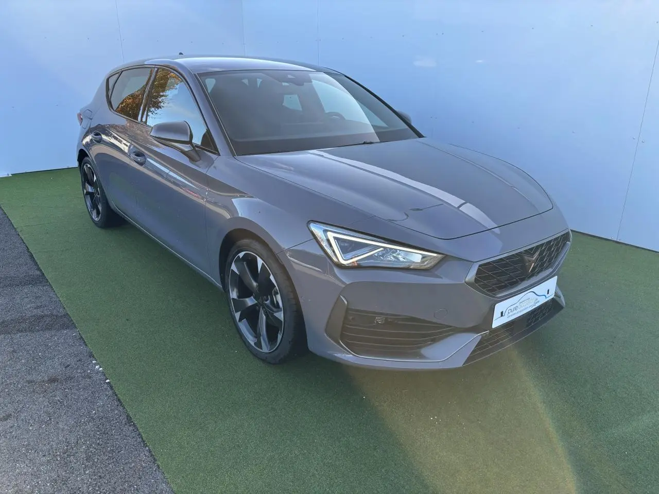 Vue 3/4 avant d'une CUPRA Leon 2024 gris Graphene avec jantes alliage noires et feux LED distinctifs.