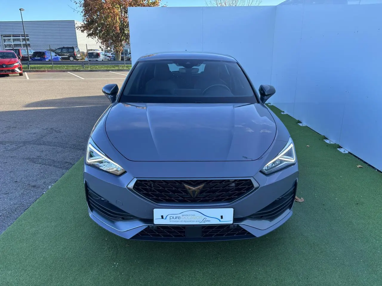Vue frontale d'une CUPRA Leon 2024 gris Graphene avec calandre noire et feux LED anguleux allumés.