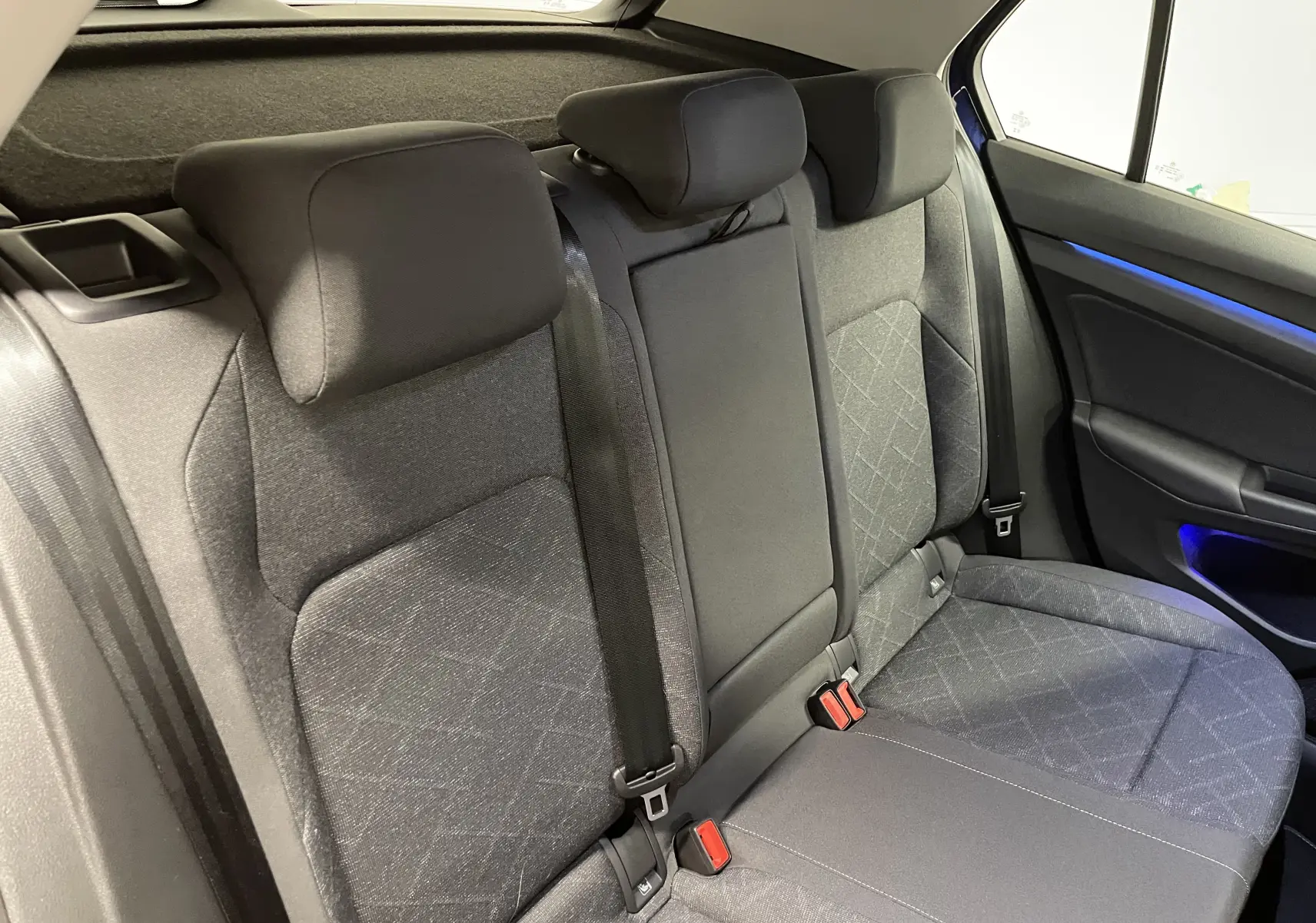 Vue rapprochée des sièges arrière en tissu gris avec ceinture et éclairage d'ambiance bleu dans une Volkswagen Golf 2023 Bleu Atlantique.