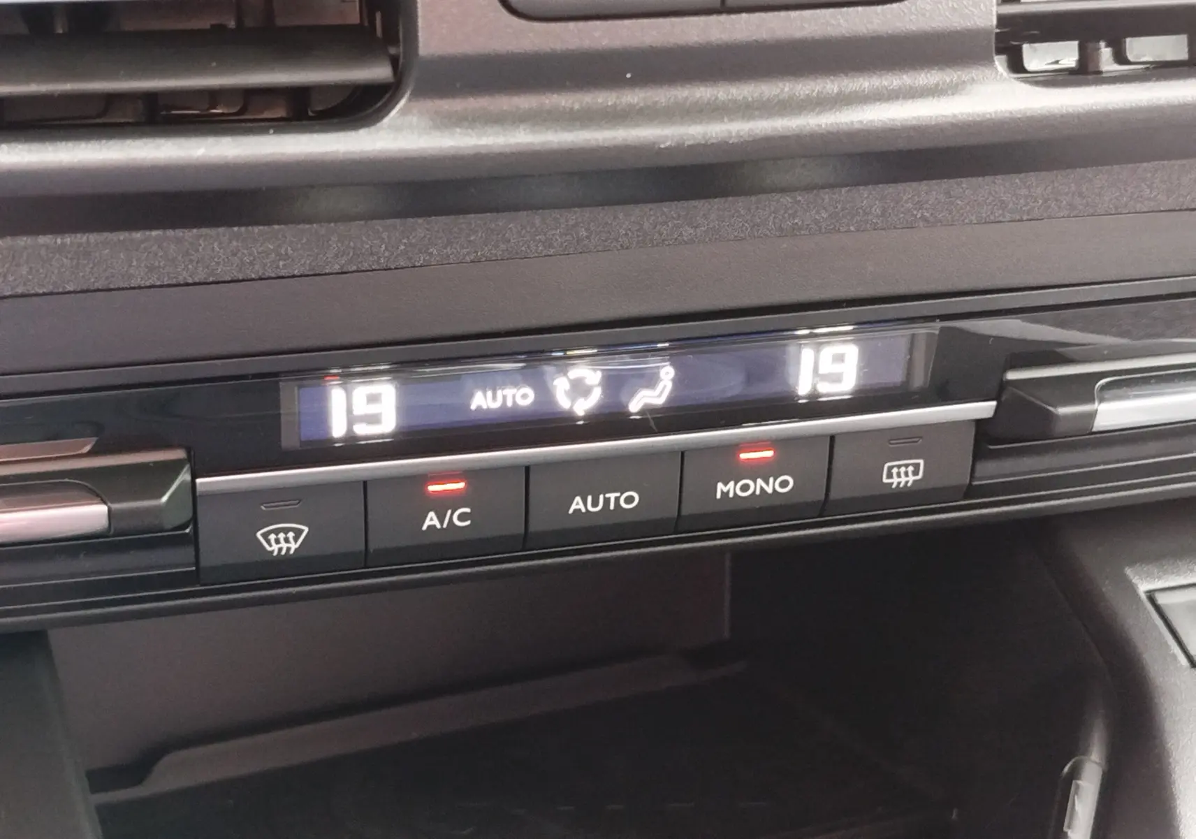Gros plan sur la commande de climatisation digitale du Peugeot Rifter noir Perla Nera, affichant 19°C en mode auto.