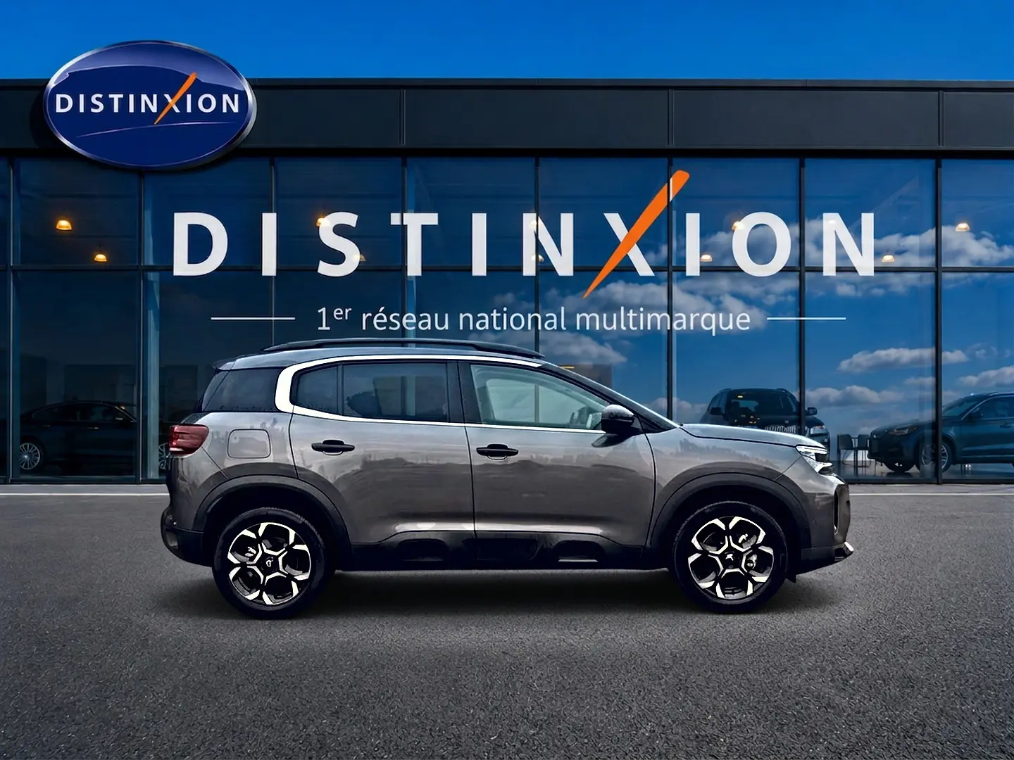 Profil droit du Citroën C5 Aircross gris platinium 2025, avec jantes alu et barres de toit visibles devant vitrine Distinxion.
