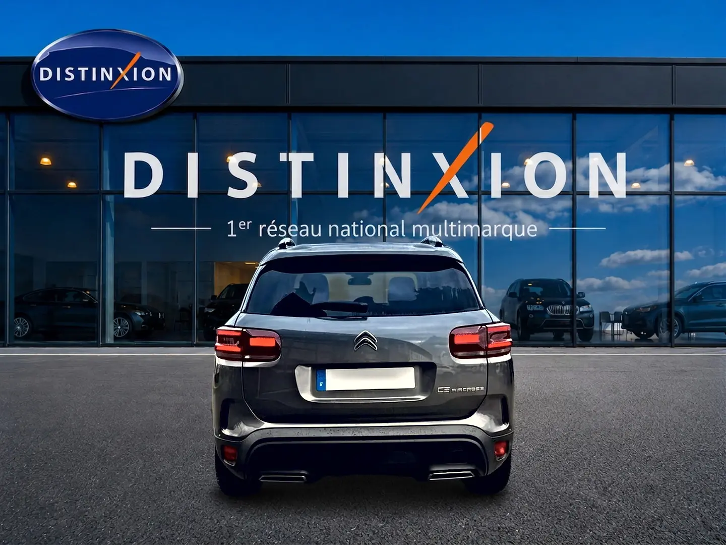 Vue arrière d'un Citroën C5 Aircross gris platinium garé devant une vitrine avec logo Distinxion.
