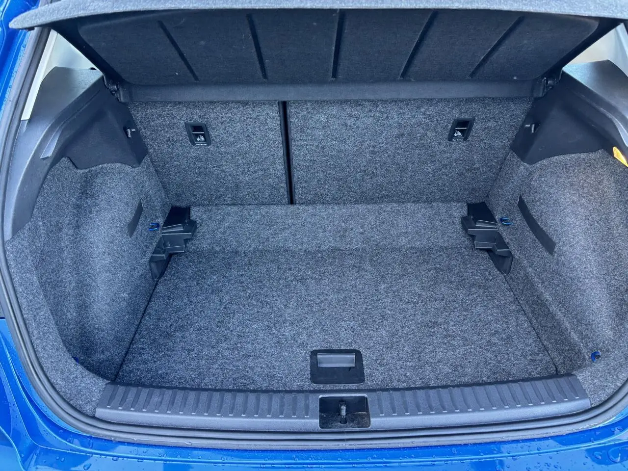 Coffre ouvert vu de l'arrière d'un SEAT Arona bleu saphir avec intérieur de coffre en moquette grise.