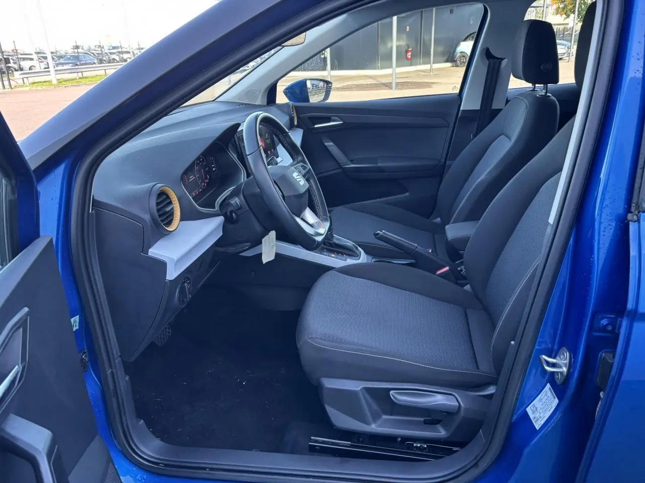 Vue intérieure côté conducteur d'une SEAT Arona bleu saphir 2024 avec sièges tissu et volant multifonction cuir.