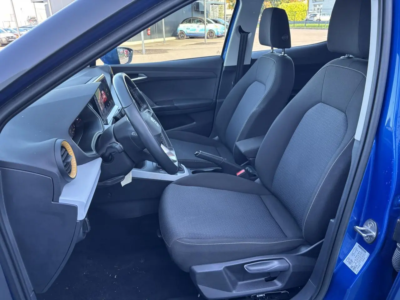 Vue intérieure côté conducteur du SEAT Arona bleu saphir, montrant les sièges tissu et le tableau de bord avec écran tactile.