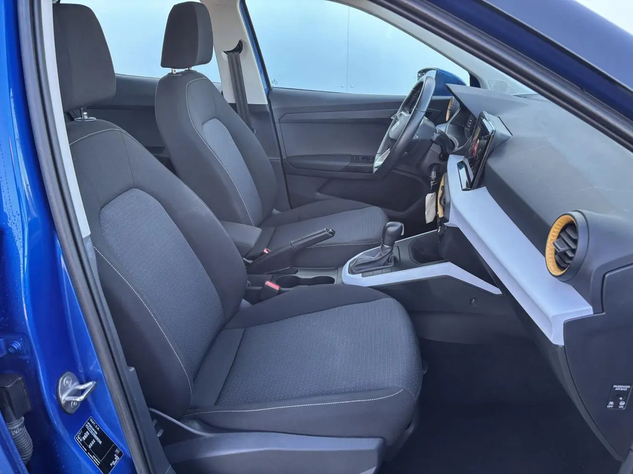 Vue intérieure côté conducteur de la SEAT Arona bleu saphir, montrant les sièges tissu et la console centrale moderne.