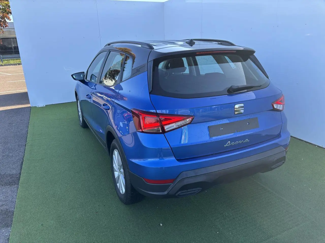 Vue 3/4 arrière d’un SEAT Arona bleu saphir avec toit noir, jantes alliage et barres de toit noires.