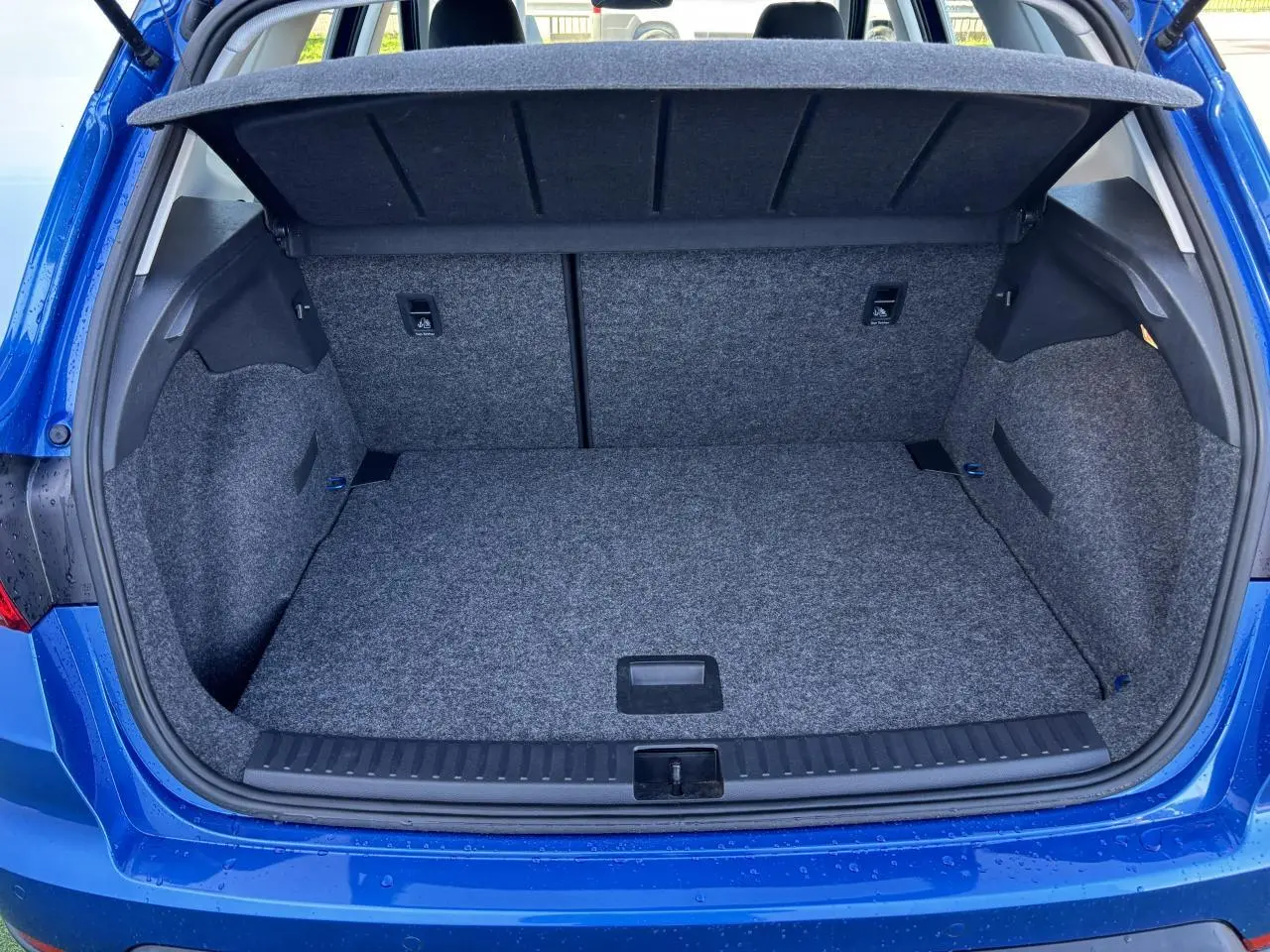 Coffre ouvert vu de l'arrière d'un SEAT Arona bleu saphir avec intérieur gris et cache-bagages relevé.