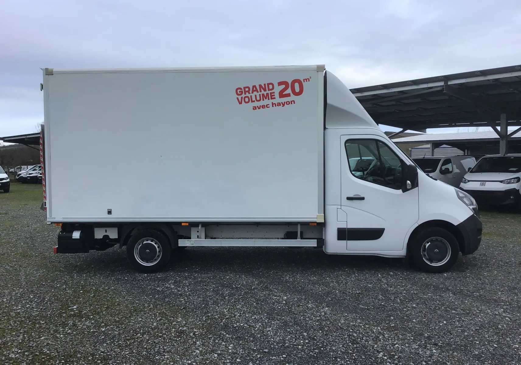 Vue de profil droit d’un utilitaire blanc Opel Movano L3H1 avec caisse volume 20 m³ et hayon électrique, stationné sur sol gravillonné.