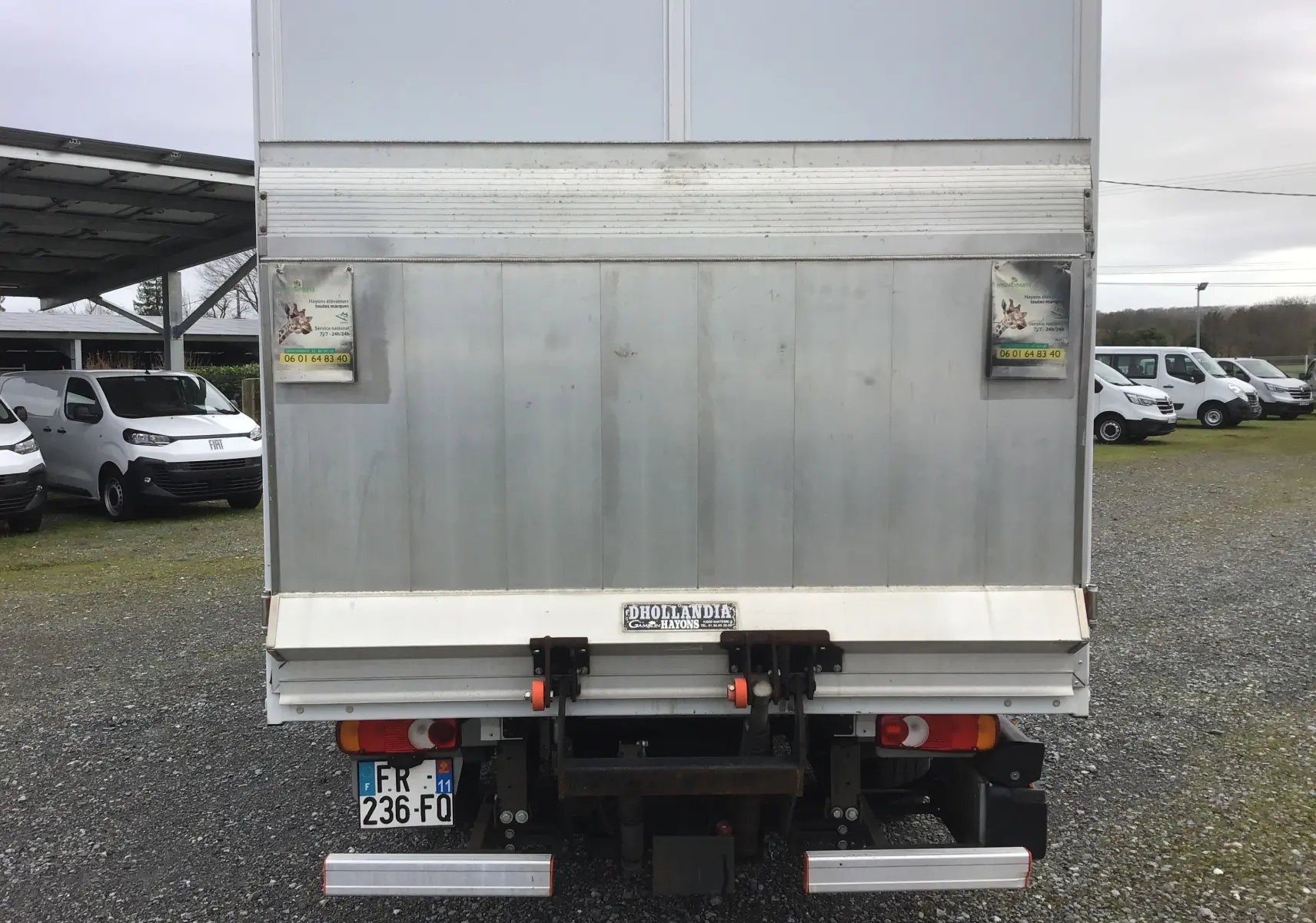 Vue arrière d’un Opel Movano blanc avec hayon électrique et caisse fermée, stationné sur un sol gravillonné.