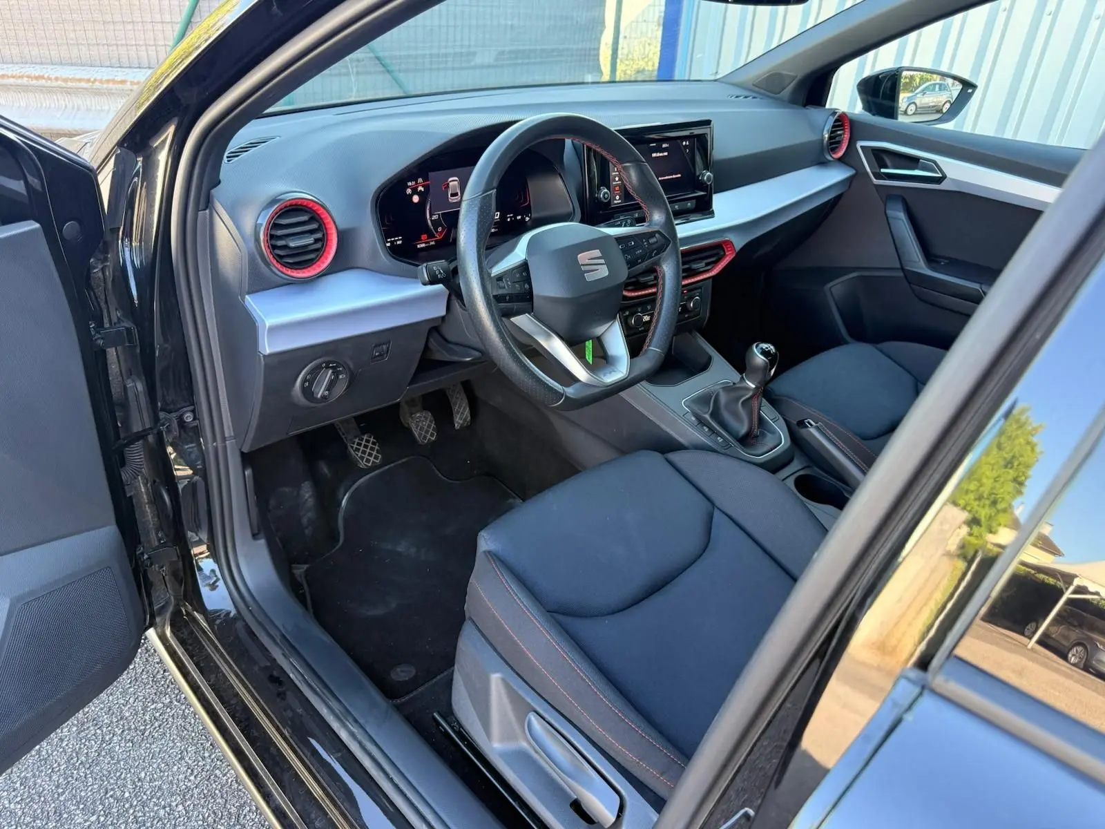 Intérieur côté conducteur d’une SEAT Ibiza noire 2025, volant cuir, détails rouges autour des aérateurs et écran tactile central.